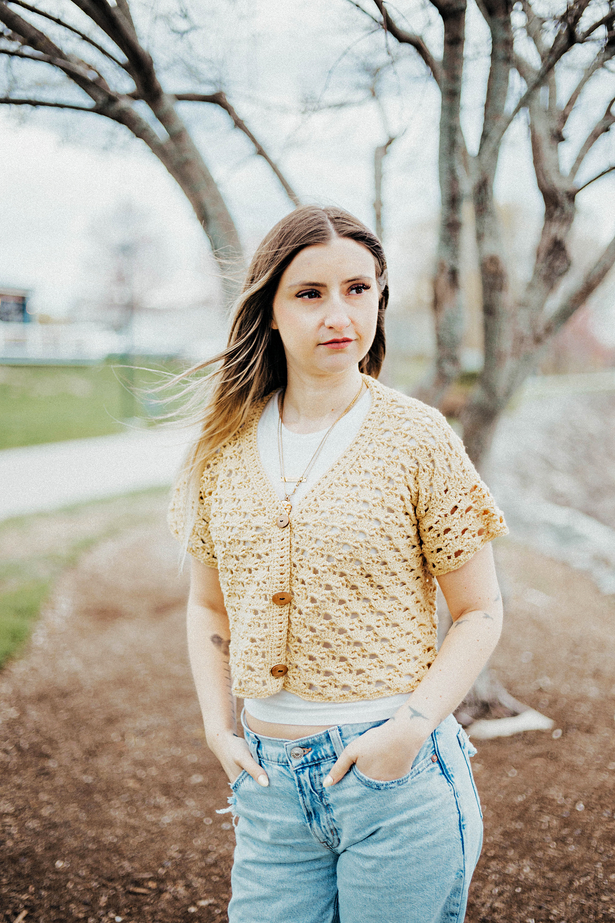 Girl wearing a beige colored cropped crochet cardigan and blue jeans standing in a yard.