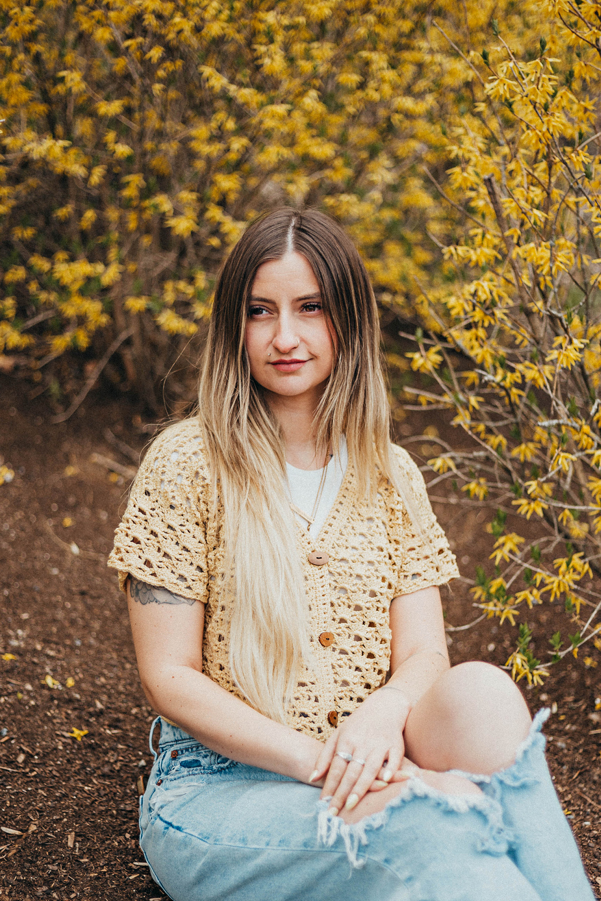 Girl wearing a beige colored cropped crochet cardigan and blue jeans sitting outside.