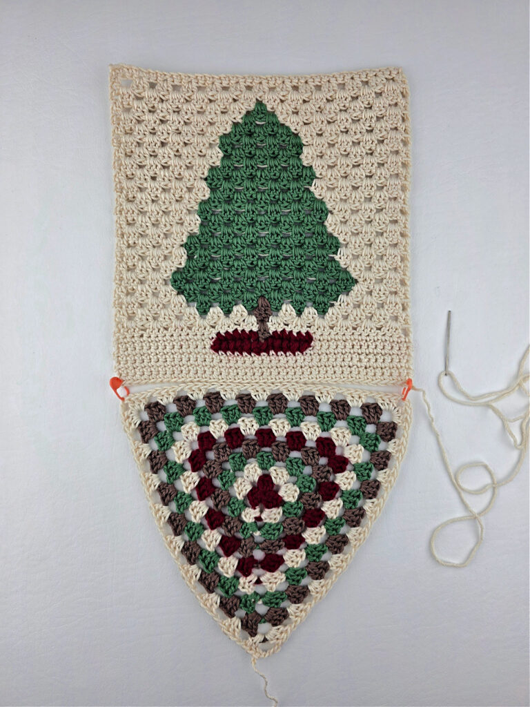 A granny triangle and fir tree made from green, red, brown, and cream yarn.