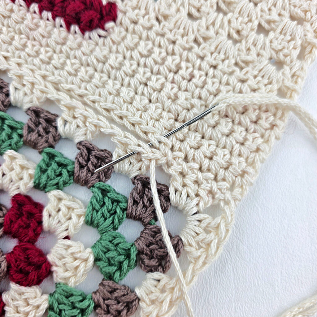 A granny triangle being attached to a white crochet piece.