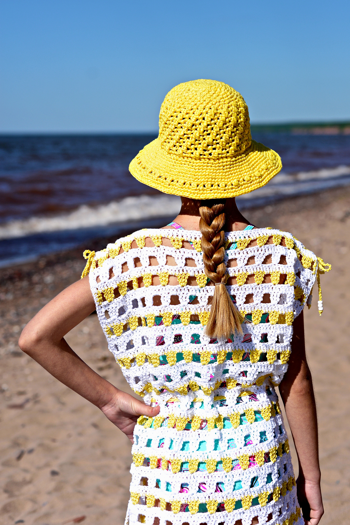 Girl modeling a white and yellow crochet beach cover up and yellow sunhat at the beach.