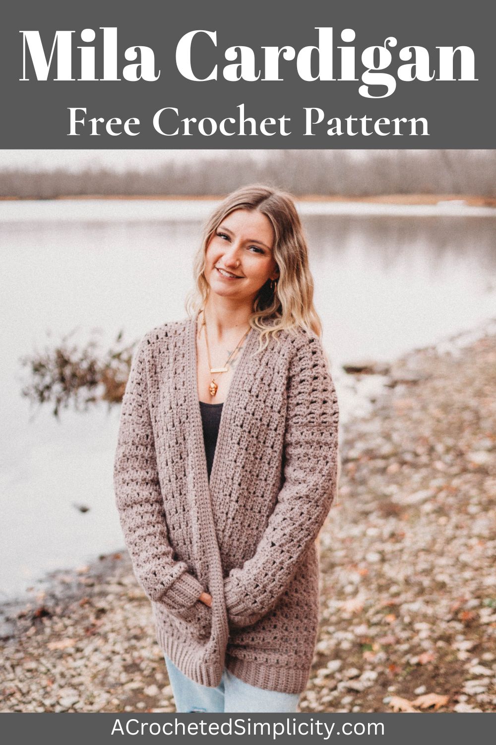 A woman with blonde hair wearing a brown crochet cardigan sweater standing in front of the water.