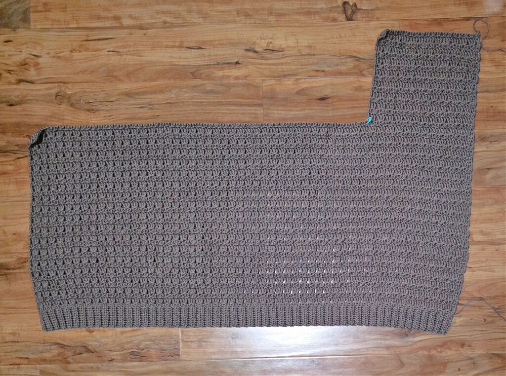 The body of cardigan crocheted with the first upper panel completed and laid flat on a floor.