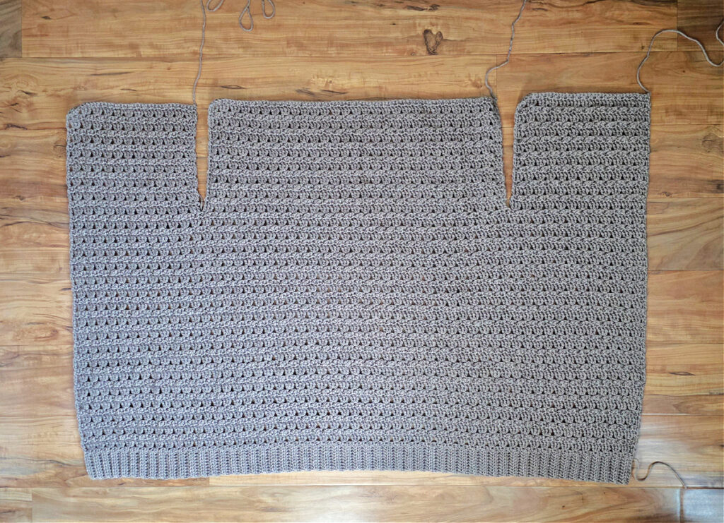 The body of cardigan crocheted with all three upper panels completed and laid flat on a floor.