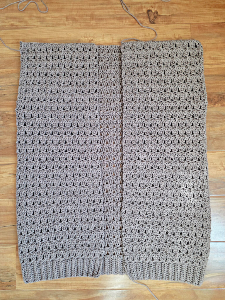 The main body of a cardigan crocheted and laid flat on a wood floor ready to add sleeves.