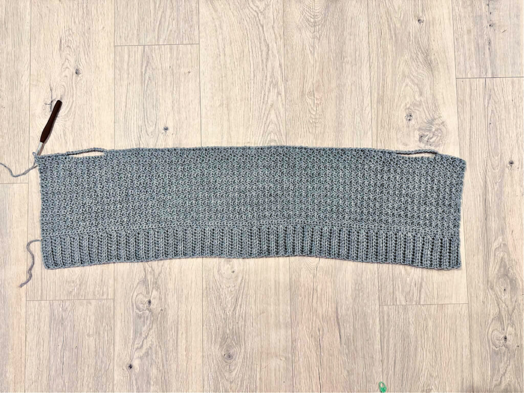 A grey crochet panel against a wooden background.