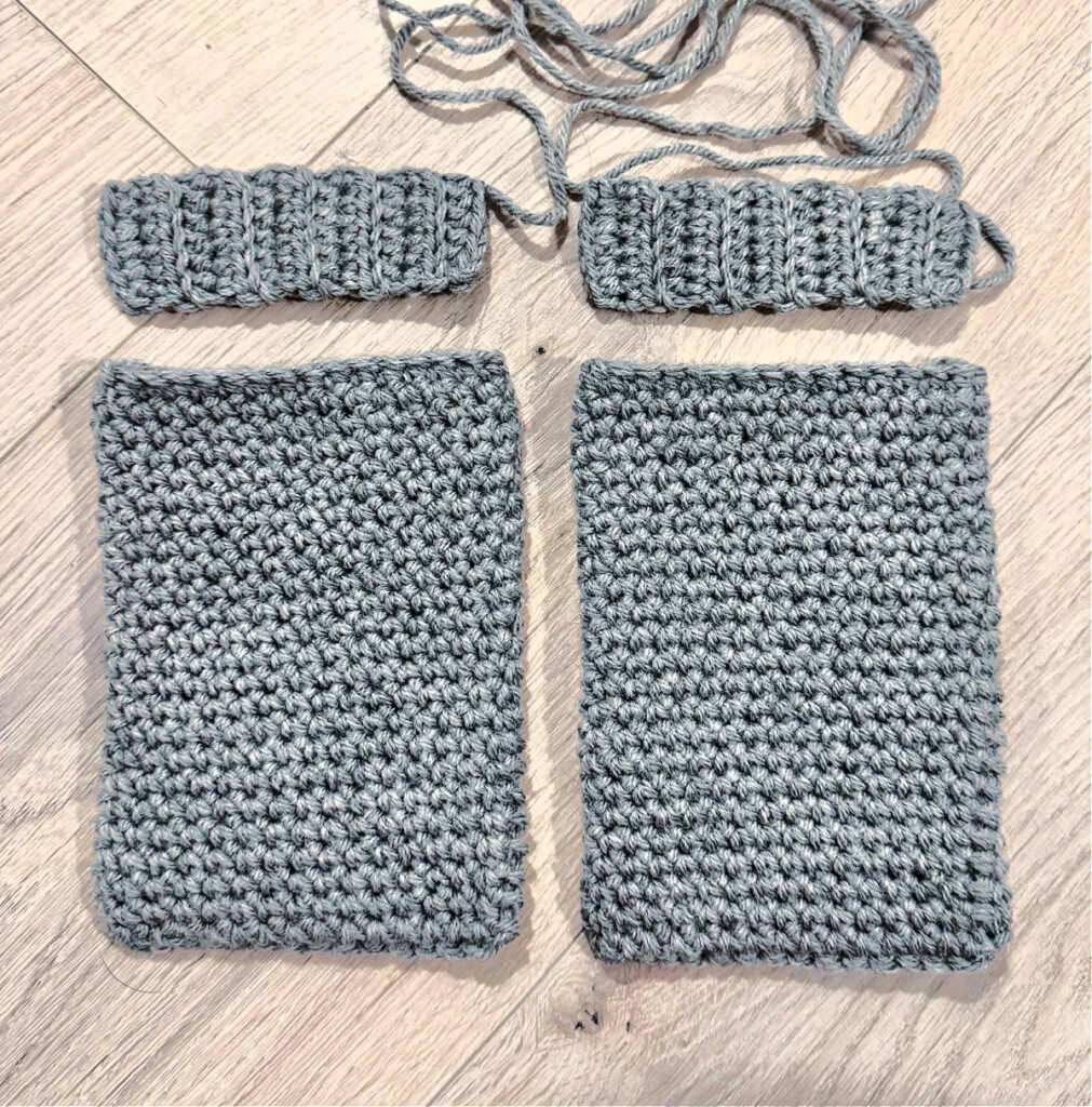 A grey crochet cardigan in progress against a wooden background.