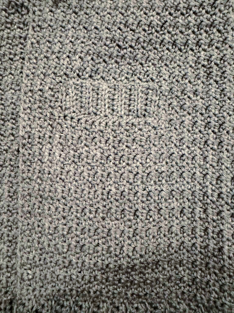 Pocket of a grey crochet cardigan.
