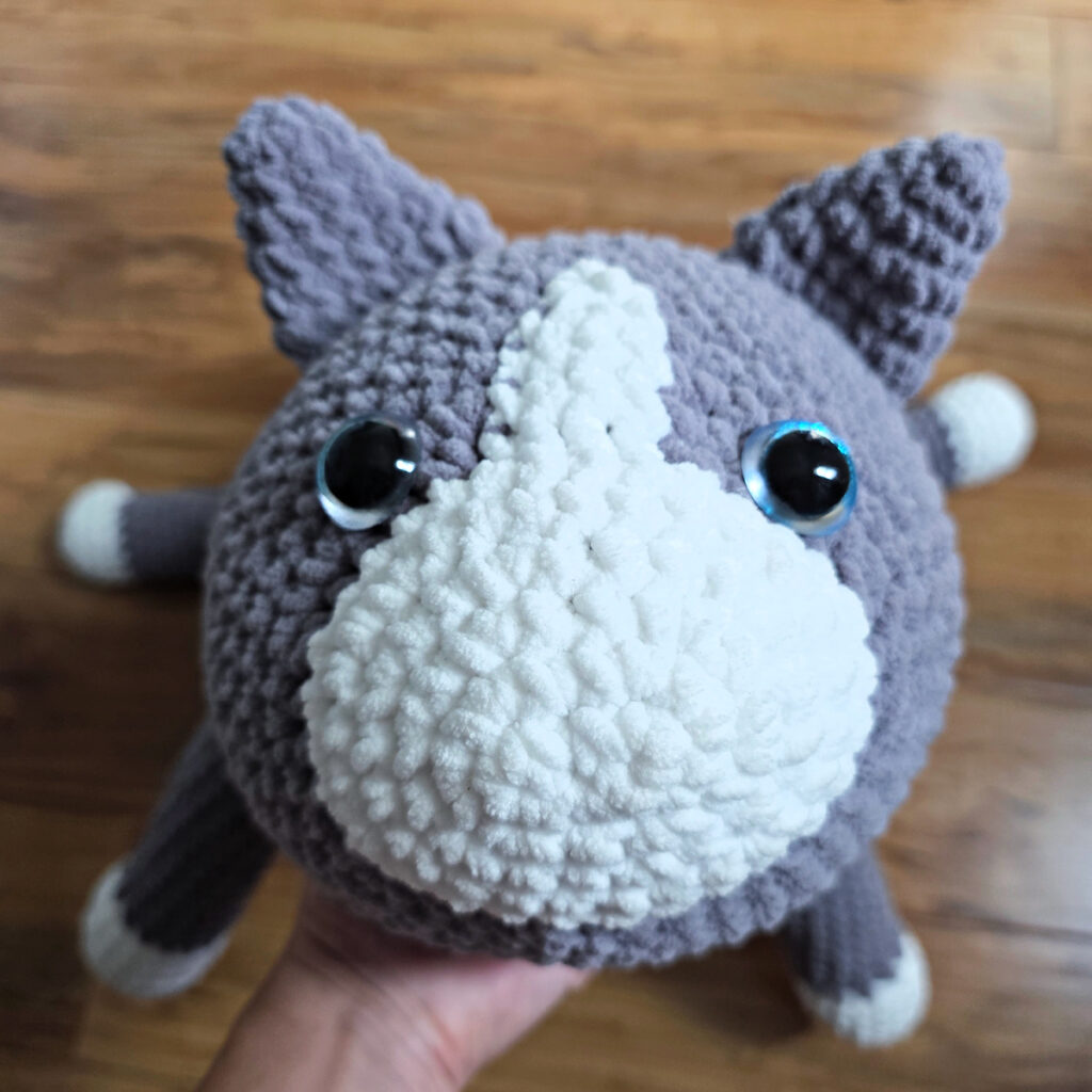 In process of assembling a crochet cat laying against a wooden floor.
