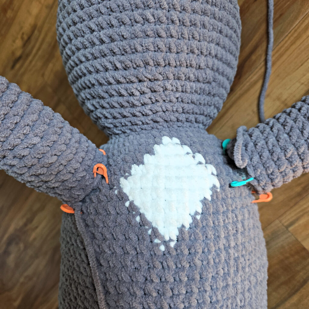 In process of assembling a crochet cat laying against a wooden floor.