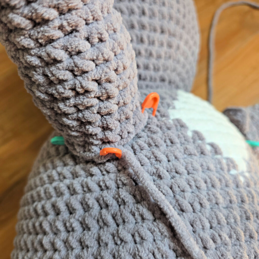 In process of assembling a crochet cat laying against a wooden floor.