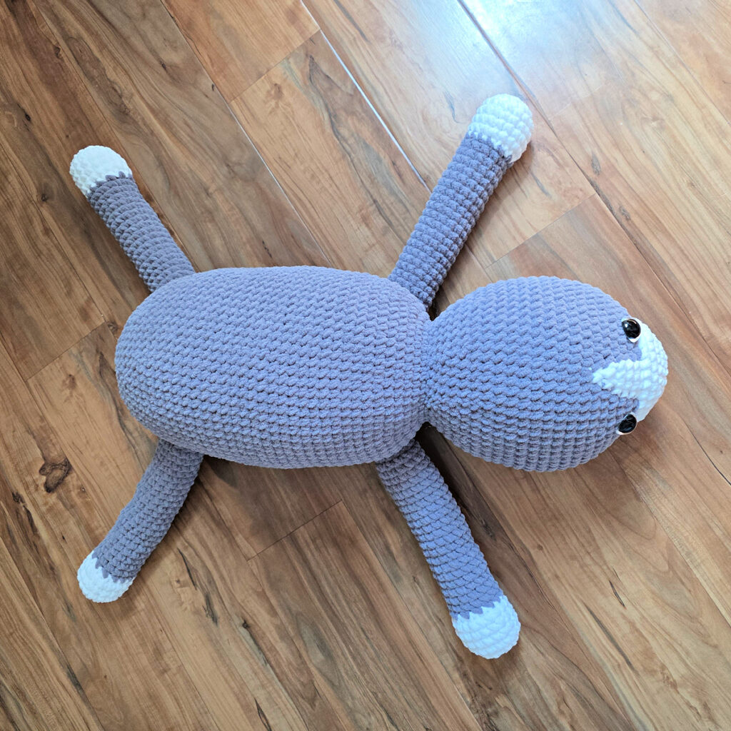 In process of assembling a crochet cat laying against a wooden floor.