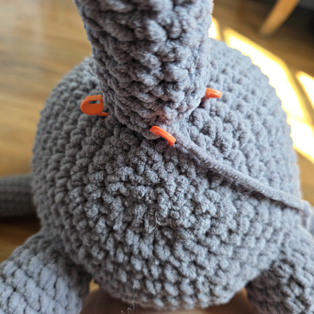 In process of assembling a crochet cat laying against a wooden floor.