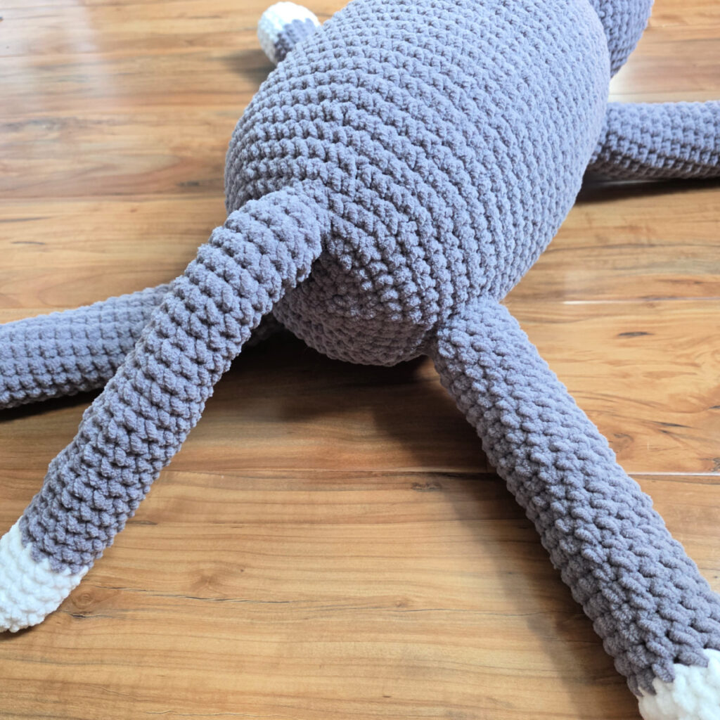 In process of assembling a crochet cat laying against a wooden floor.