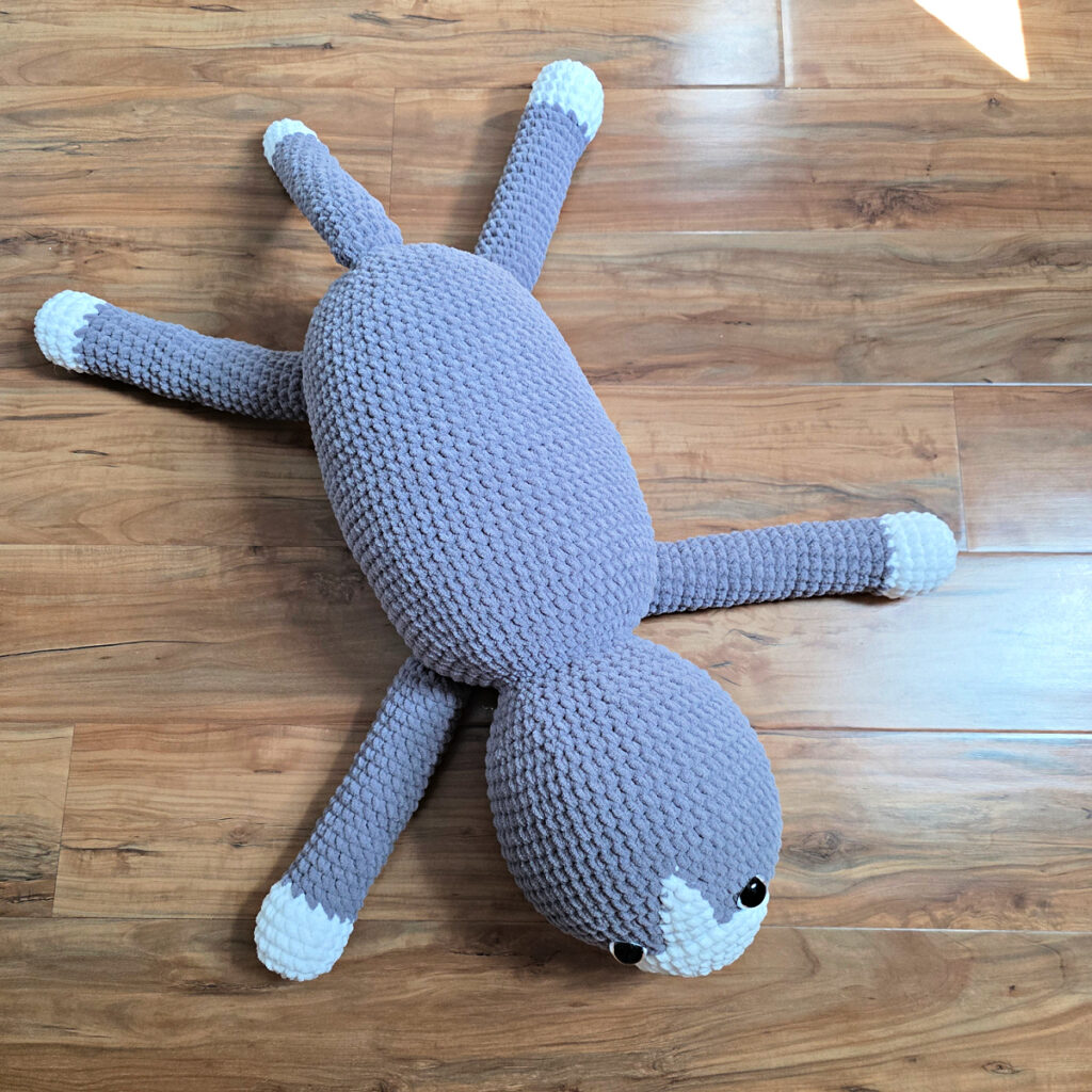 In process of assembling a crochet cat laying against a wooden floor.