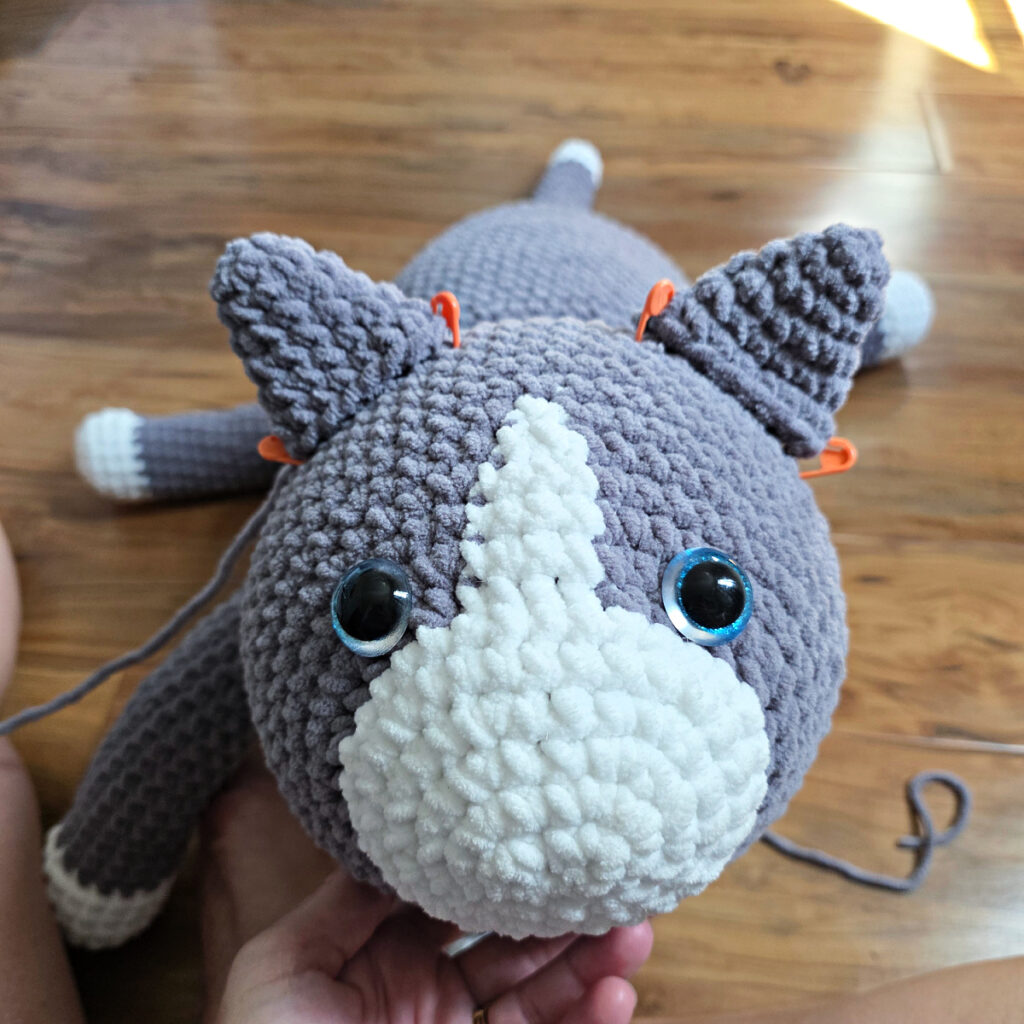 In process of assembling a crochet cat laying against a wooden floor.