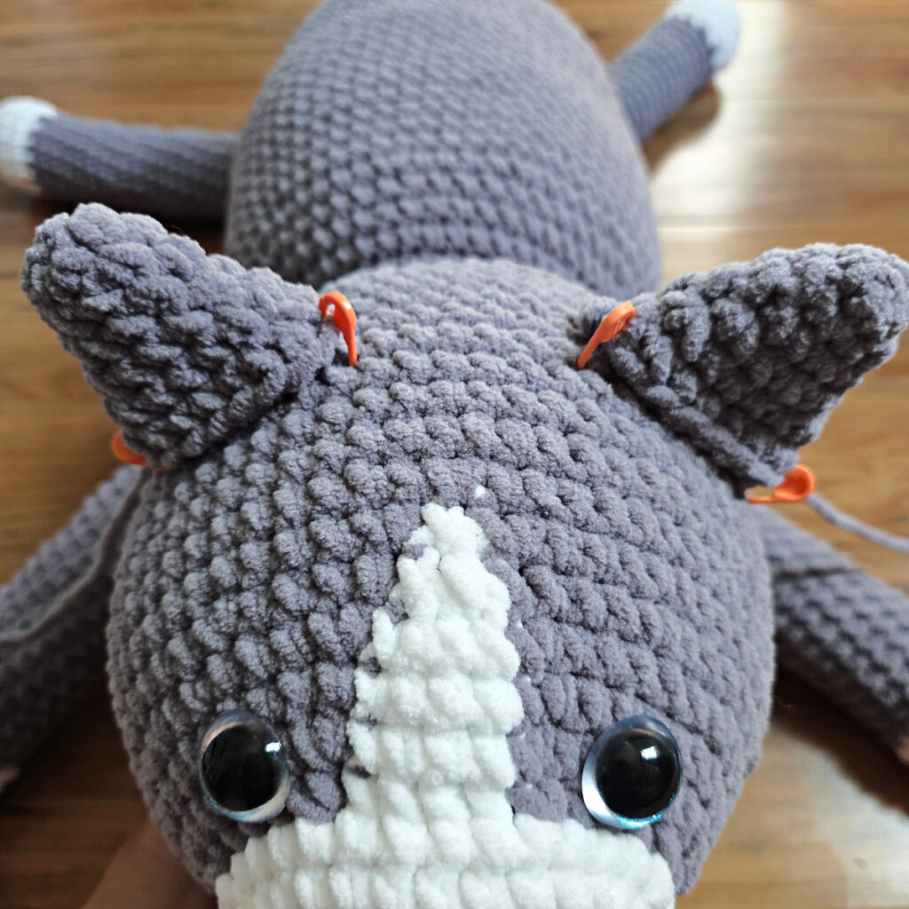In process of assembling a crochet cat laying against a wooden floor.