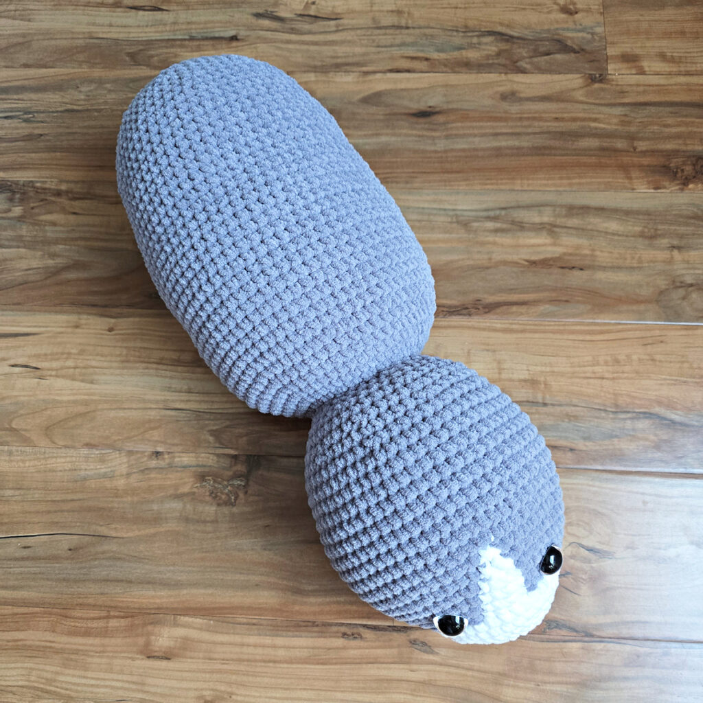 In process of making a crochet cat laying against a wooden floor.