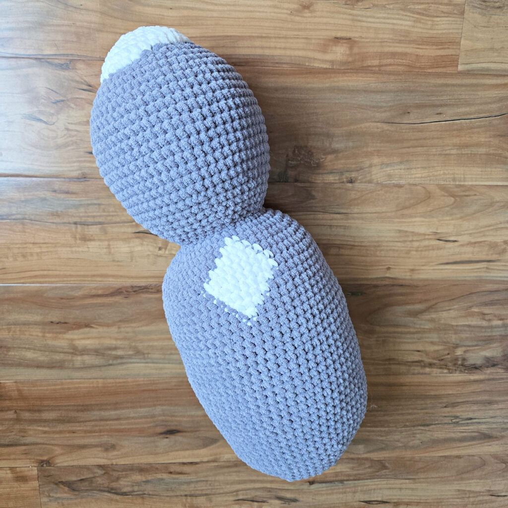 In process of making a crochet cat laying against a wooden floor.