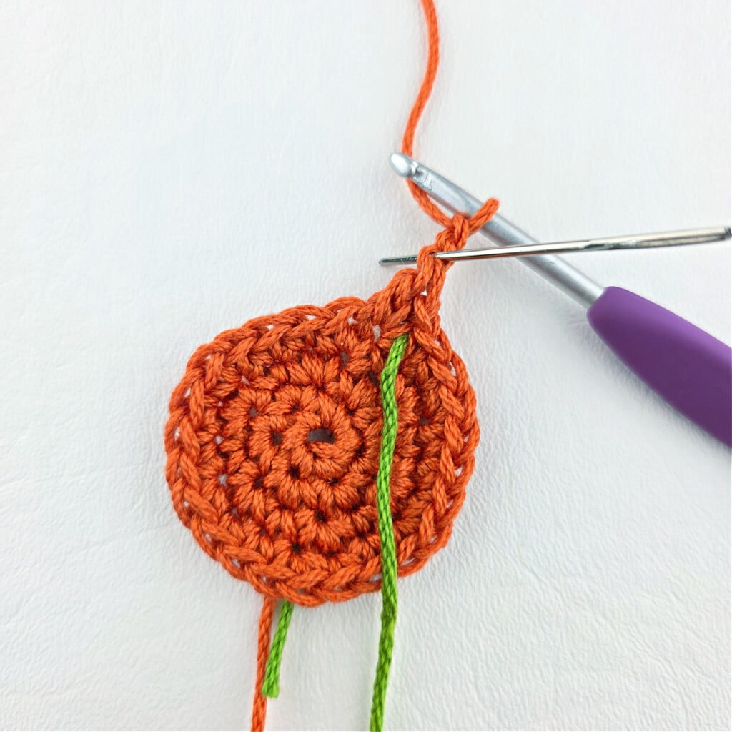 An orange crochet circle with a purple crochet hook.
