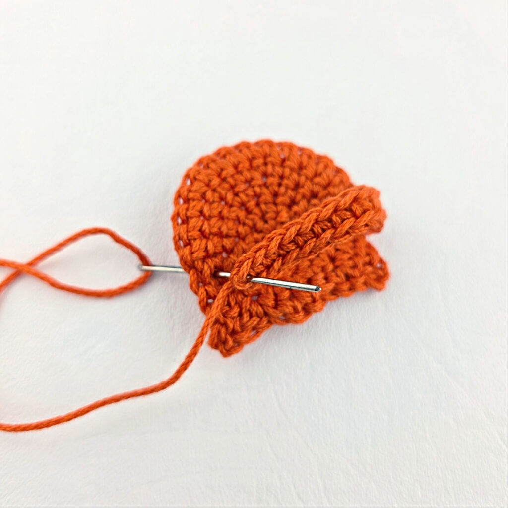 Seaming the back of an orange crochet cat bookmark.