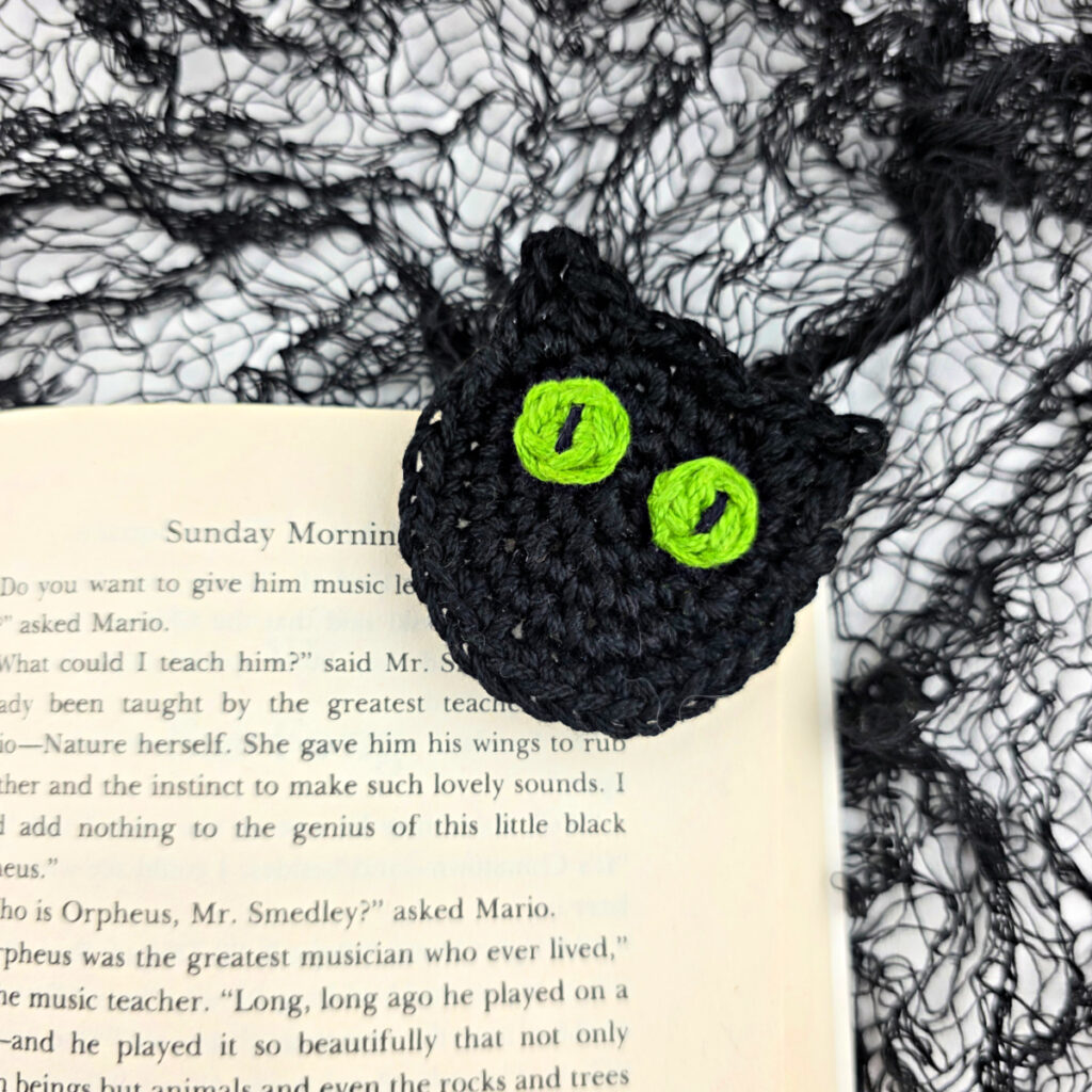 A crochet cat bookmark attached to a book.