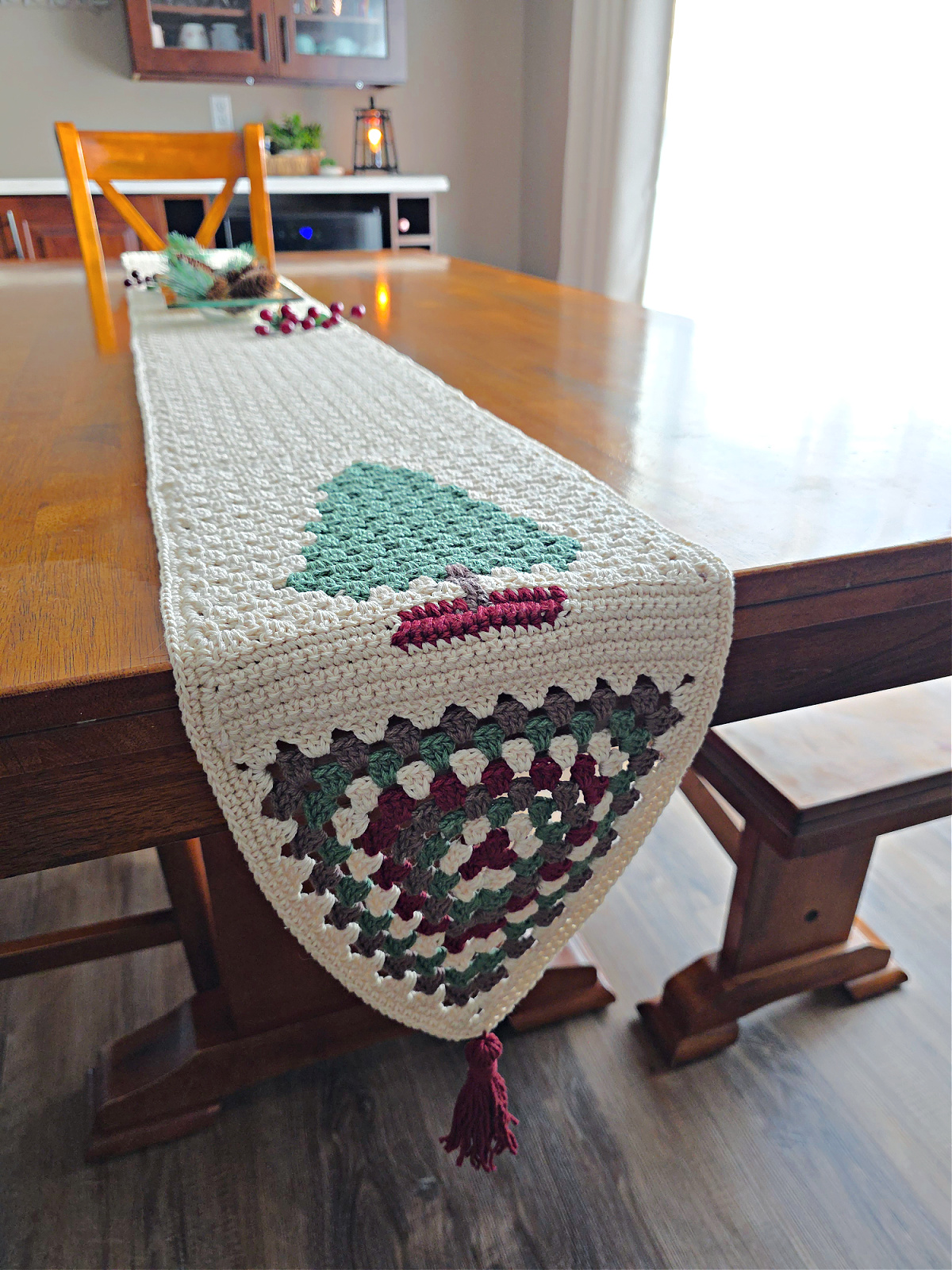 Crochet christmas table runner on a wooden table with a fir tree and granny triangle at the ends.