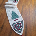 Crochet table runner on a wooden table with a fir tree and granny triangle at one end.