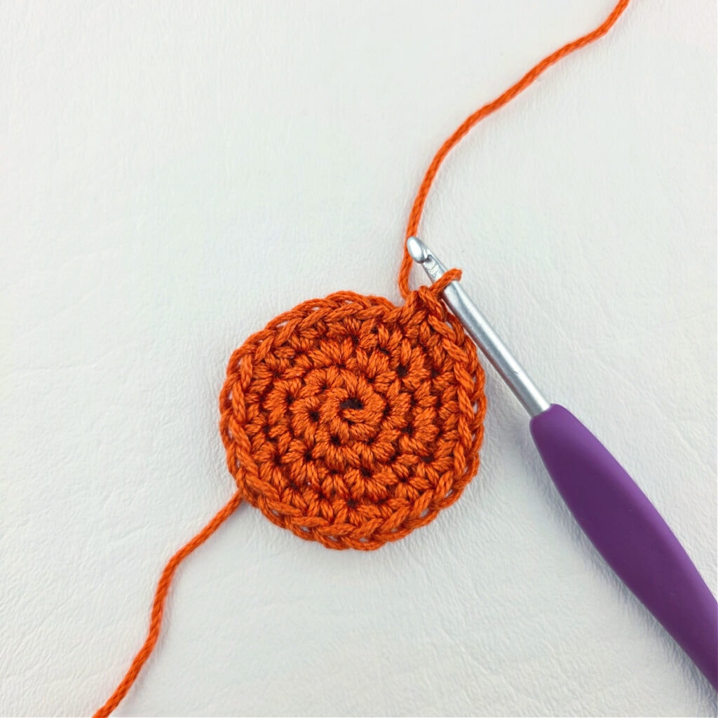 An orange crochet circle with a purple crochet hook.