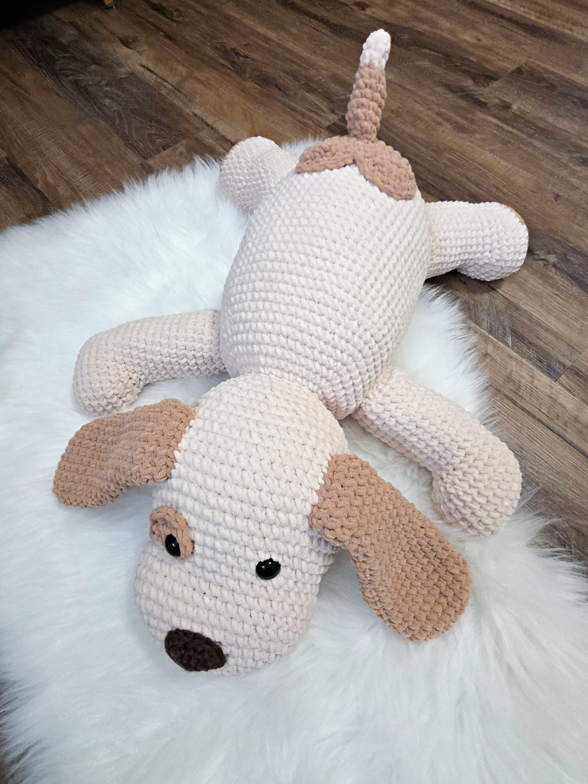 A large plush white and brown crochet dog on a faux fur carpet.