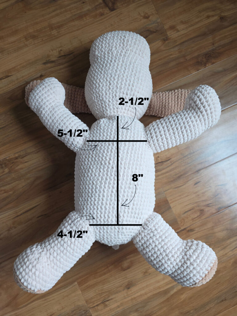 A crochet dog laying on his back to show measurements of where to attach the legs.
