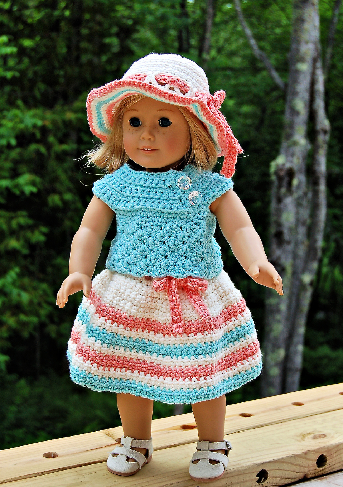 An 18" doll wearing a colorful crochet doll dress with a sunhat.