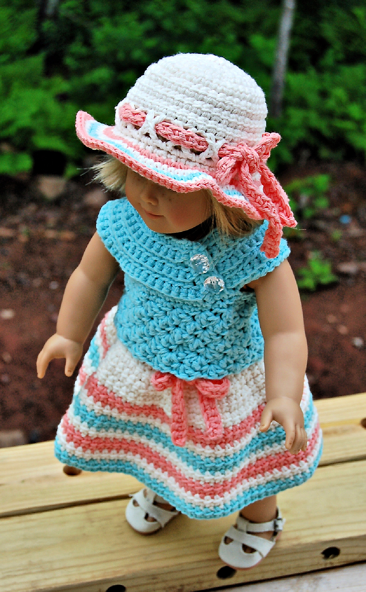 An 18" doll wearing a colorful crochet doll dress with a sunhat.