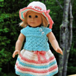 An 18" doll wearing a colorful crochet doll dress with a sunhat.