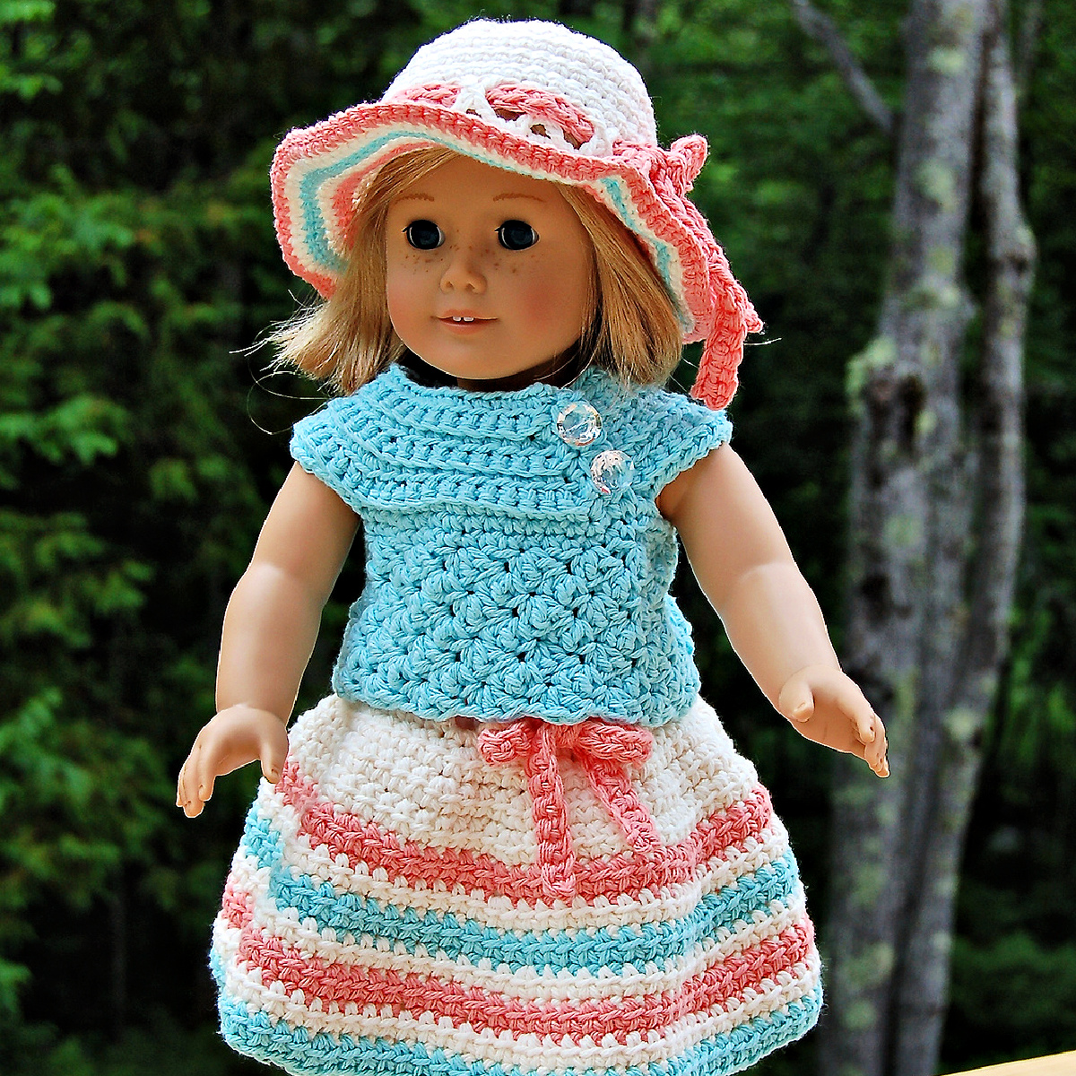 An 18" doll wearing a colorful crochet doll dress with a sunhat.