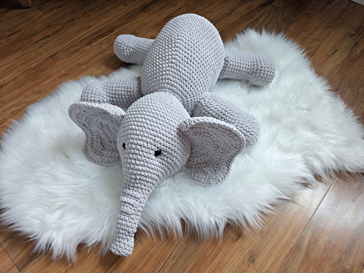 A gray crochet elephant amigurumi laying on a white plush rug.