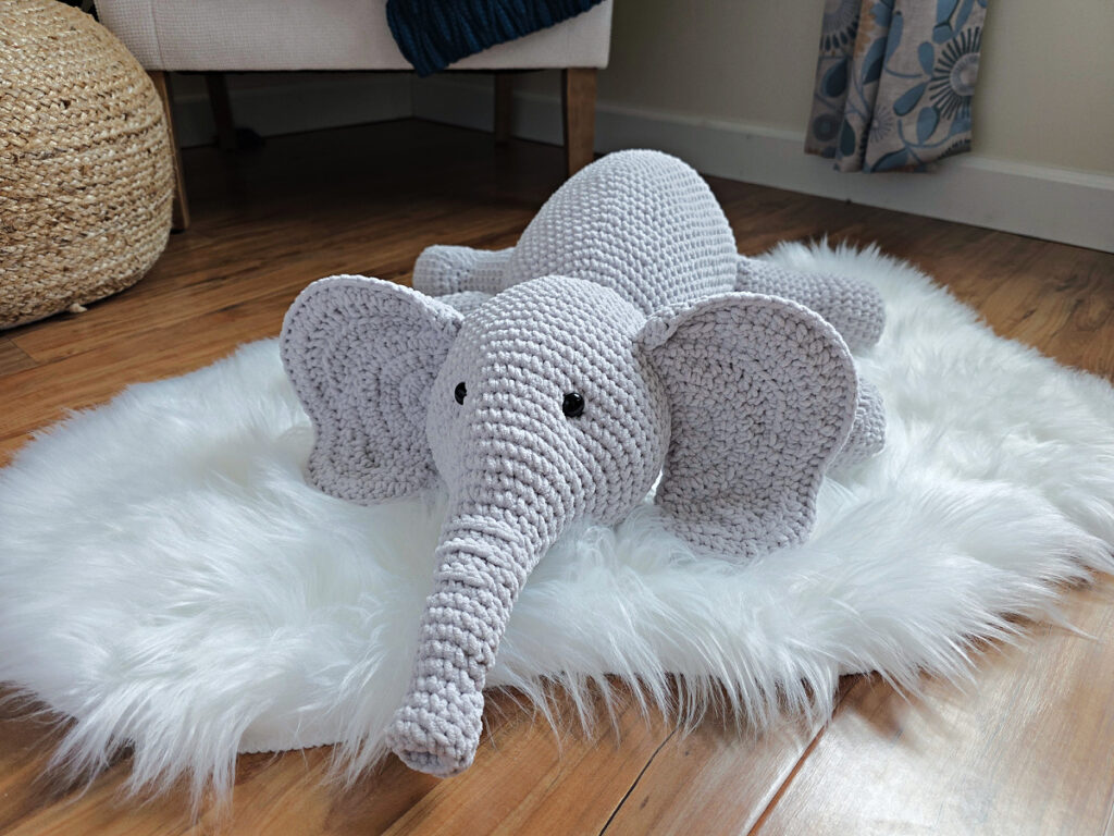 A gray crochet elephant amigurumi laying on a white plush rug.