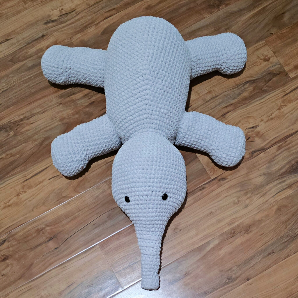 A gray crochet elephant in progress on a wooden floor.