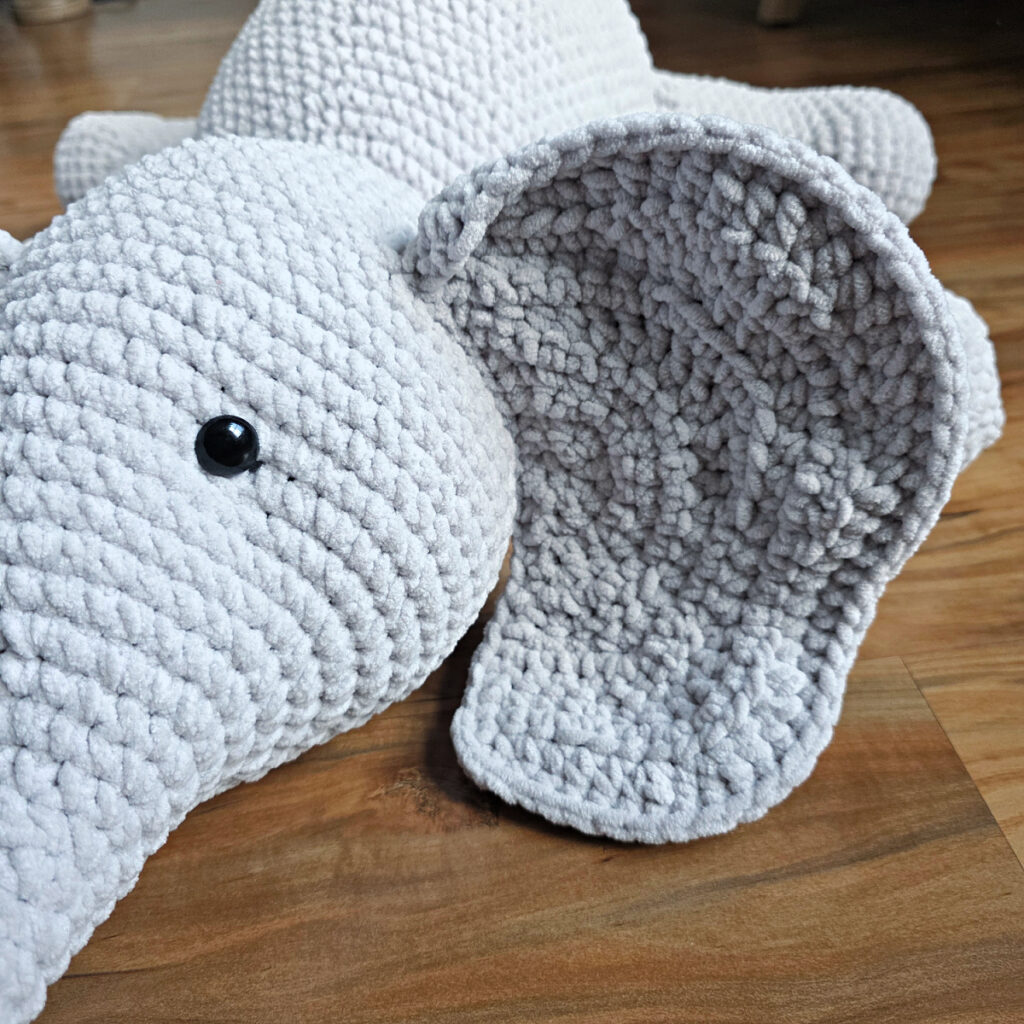 A gray crochet elephant amigurumi on a wooden floor.