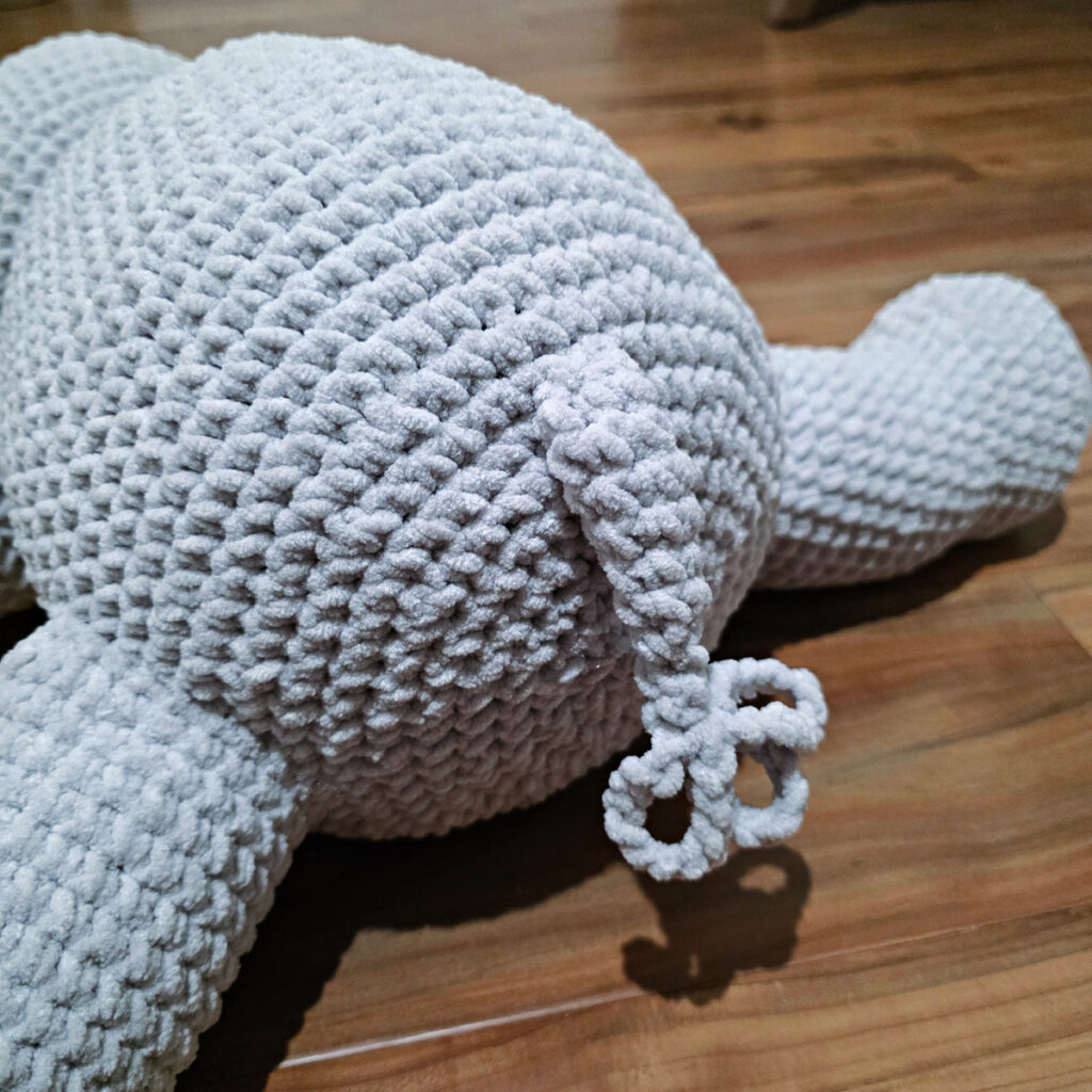 A gray crochet elephant tail attached to a body on a wooden floor.