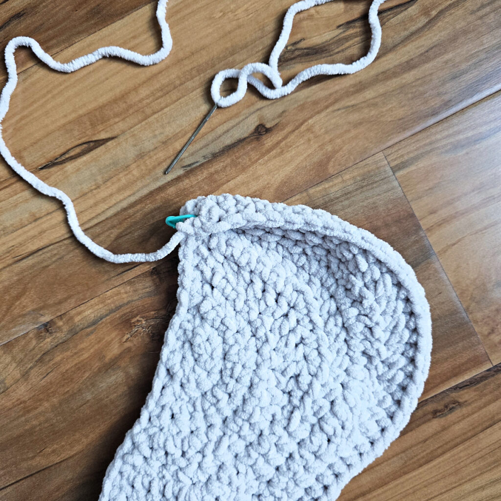 A gray crochet elephant ear in progress on a wooden floor.