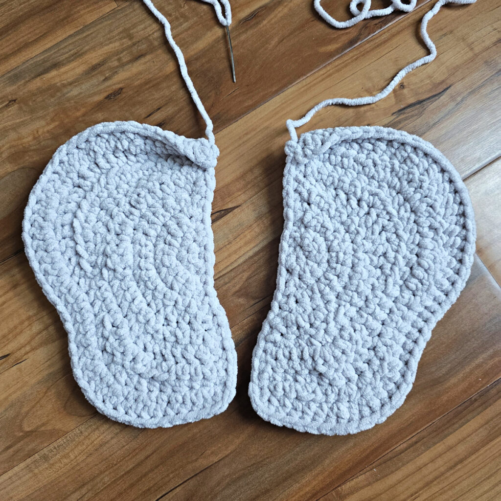 Two gray crochet elephant ears in progress on a wooden floor.