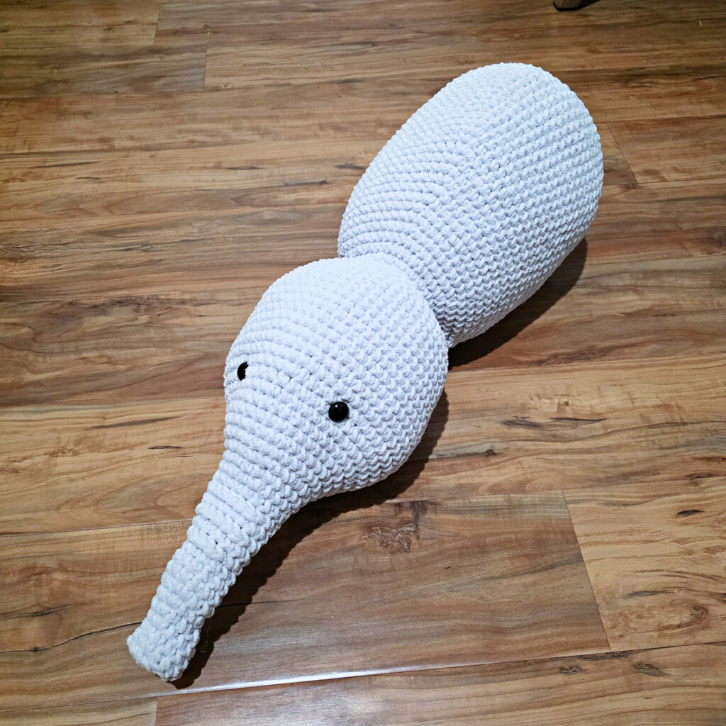 A gray crochet elephant toy in progress on a wooden floor.