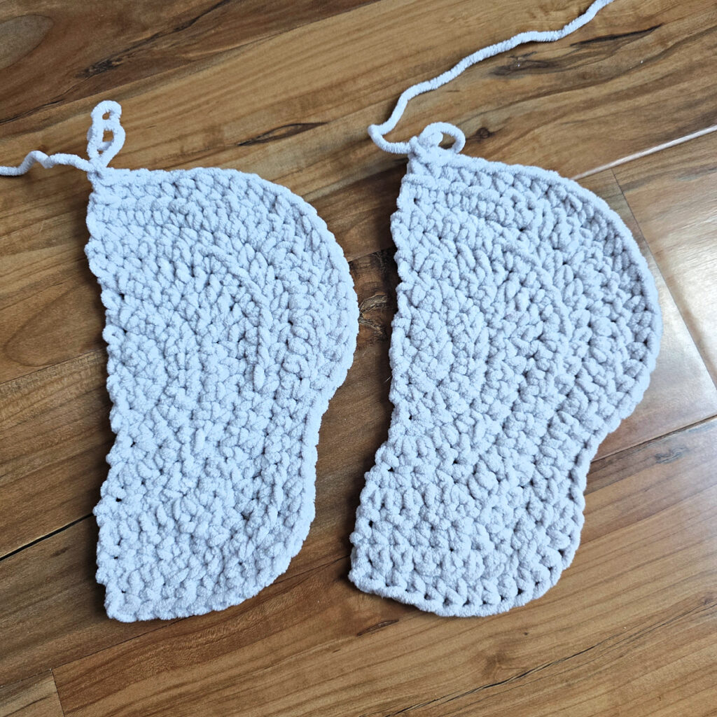 Two gray crochet elephant ears in progress on a wooden floor.