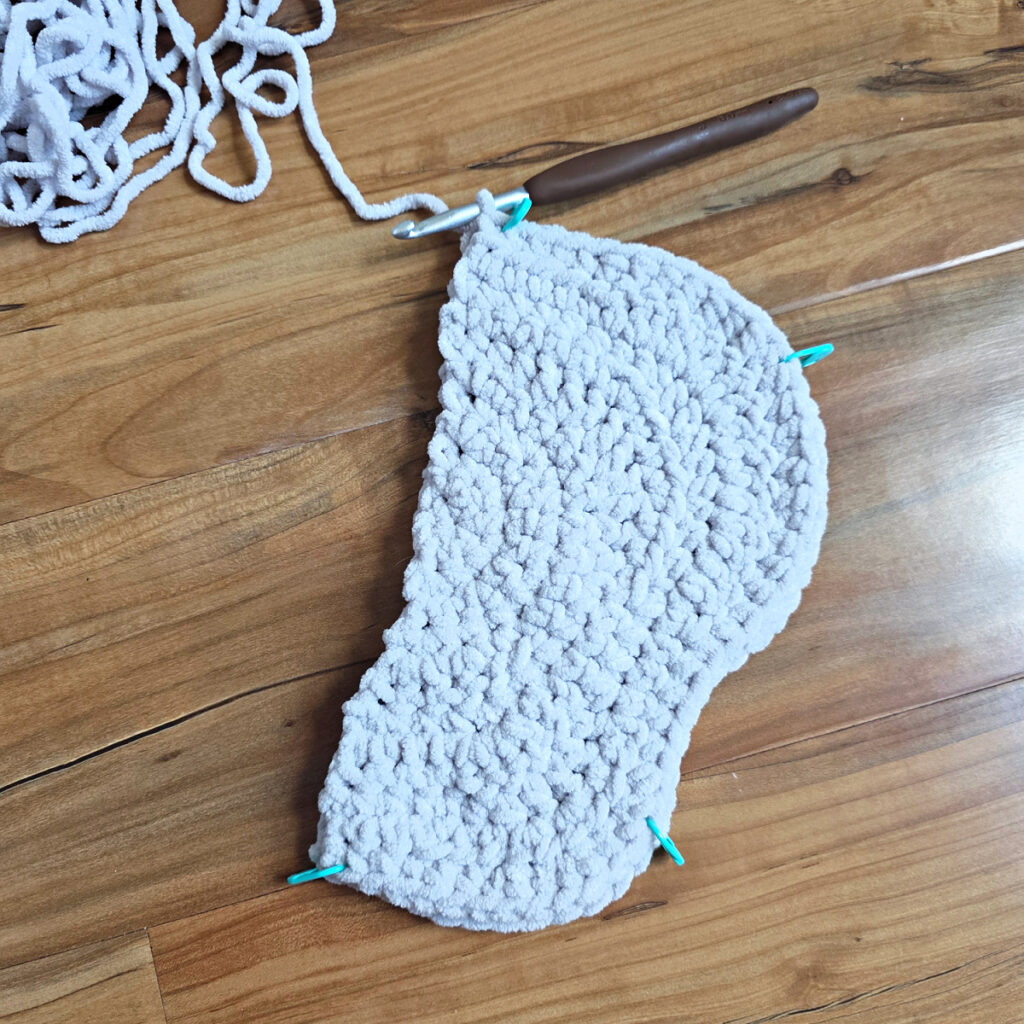 A gray crochet elephant ear in progress on a wooden floor.