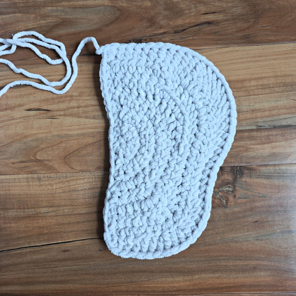 A gray crochet elephant ear in progress on a wooden floor.