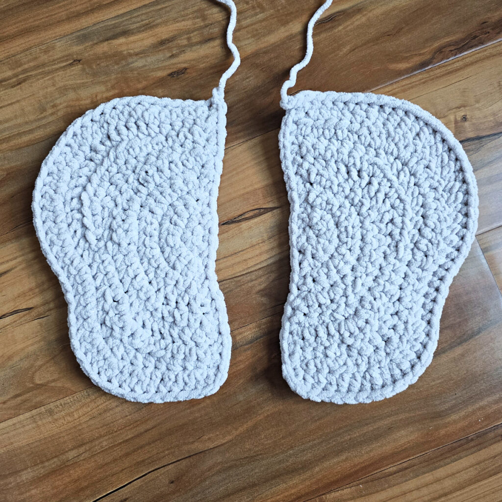 Two gray crochet elephant ears in progress on a wooden floor.