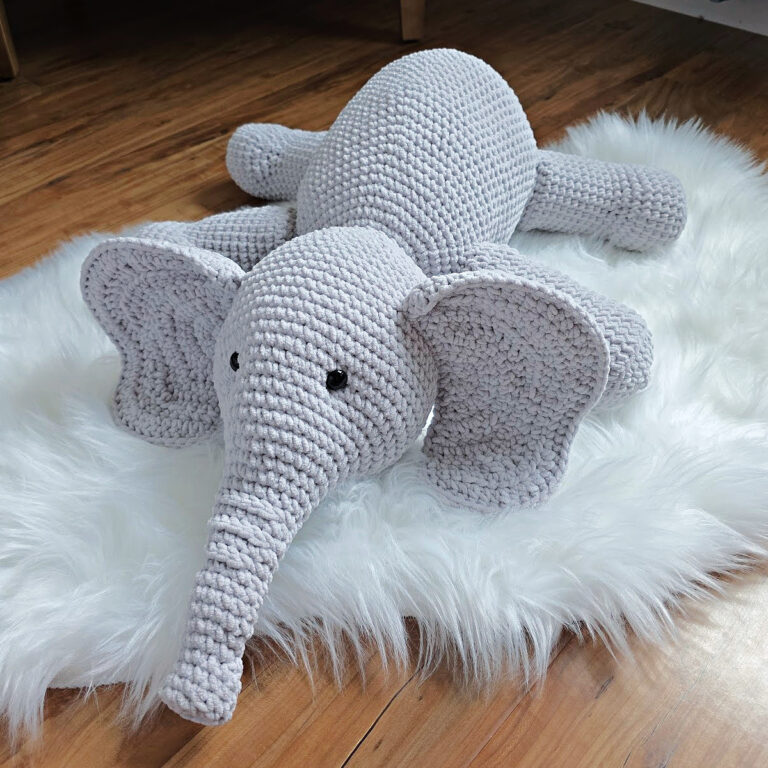 A gray crochet elephant amigurumi laying on a white plush rug.