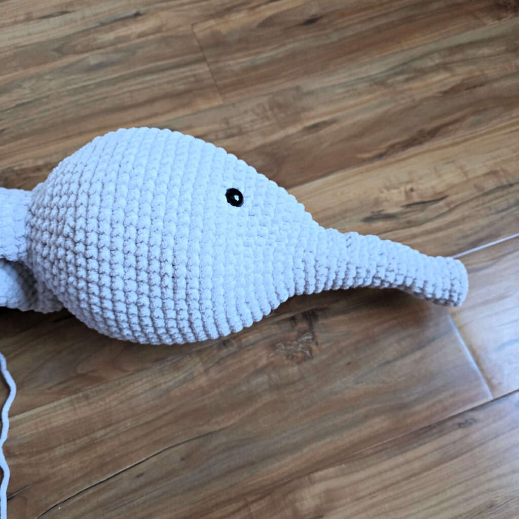 A gray crochet elephant head in progress on a wooden floor.