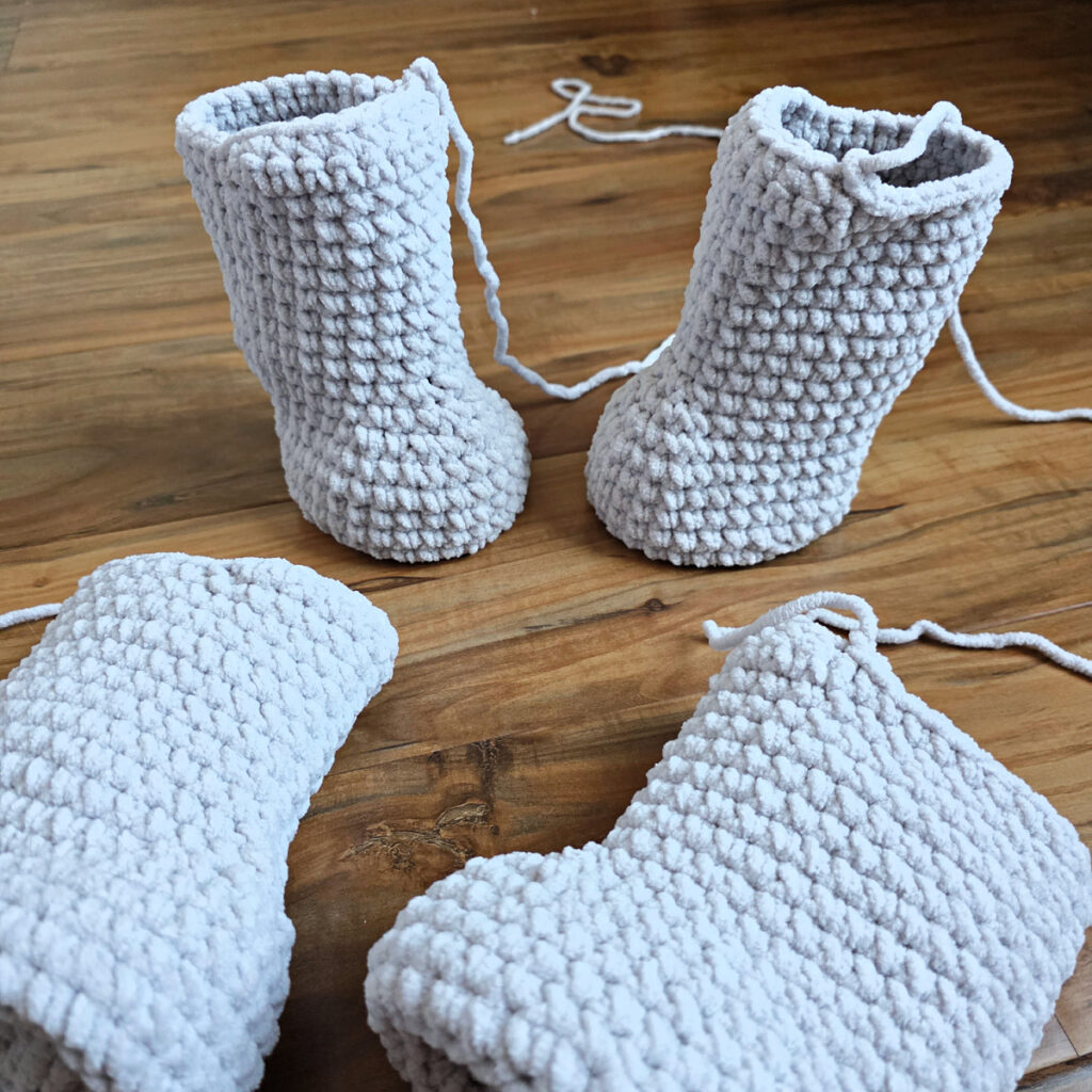 Four gray crochet amigurumi legs on a wooden floor.